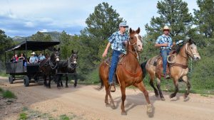 two men on horseback guide a horsedrawn shuttle with many tourist inside along a trail near Zion National Park