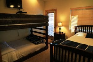 a neatly made double bed and a set of bunk beds with a mounted television inside of a vacation home at Zion Ponderosa Ranch