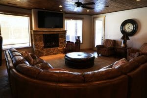 a large couch encircles a comfortable living room with a large TV and fireplace inside of a vacation home at Zion Ponderosa Ranch