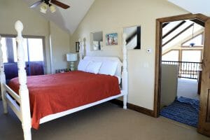 a neatly made queen sized bed with 4 white bed posts on the top floor inside a vacation home near Zion National Park