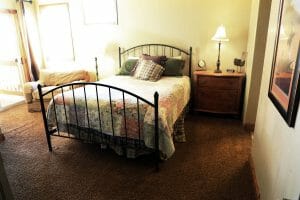 A bed room with a neatly made full sized bed, a lounge, and a balcony door in a vacation home near Zion national park