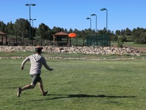 a man runs after a frisbee in a green field at zion ponderosa ranch