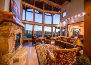 A beautiful living room with couches and chairs with a large stone fire place. The room contains a grand view of southern Utah through large glass windows!
