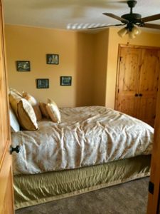 A bed is neatly made with many throw pillows in a bedroom with a wooden door to a closet