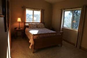 A large bed is made with a lit nightstand lamp and 2 windows