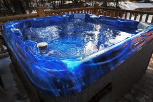 a hot tub with a blue inner shell bubbles invitingly on a deck with snow in the back ground