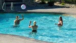 Three friends are playing with a beach ball in the large blue water pool at the Zion Ponderosa Ranch Resort