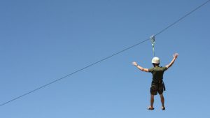 a man wearing a helmet holds out his arms while ziplining near Zion National park