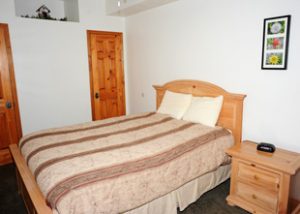 A larger bed is made in a clean room with a wooden bedframe