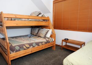 a wooden bunk bed is well made near another bed with a closed window near by