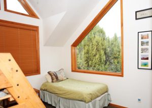 a small bed is made near bunk beds by a large window