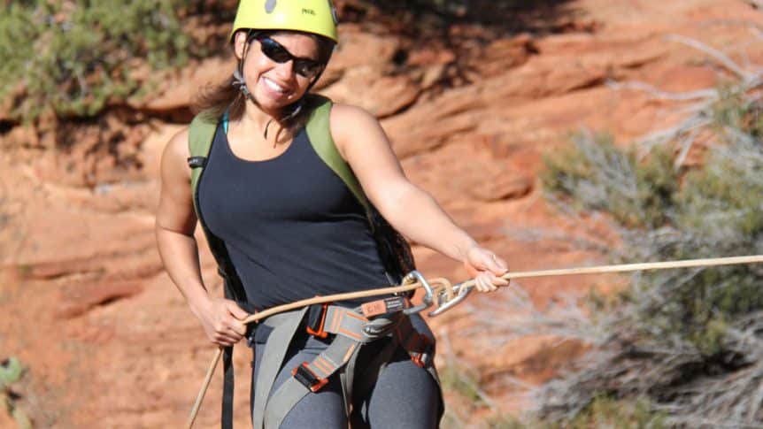a woman poses for a photo before she repels down a rock wall near zion national park