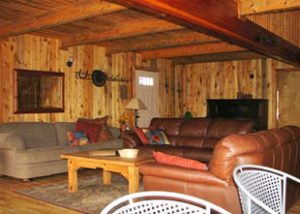 A living room in a wood paneled Livingroom has 3 couches and rustic decorations