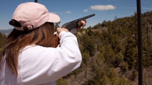 A woman with brown hair is dressed warmly and shooting a shotgun at a trap range in southern utah