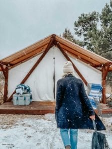 A warmly dressed woman walks toward a glamping tent in the snow at Zion Ponderosa Ranch